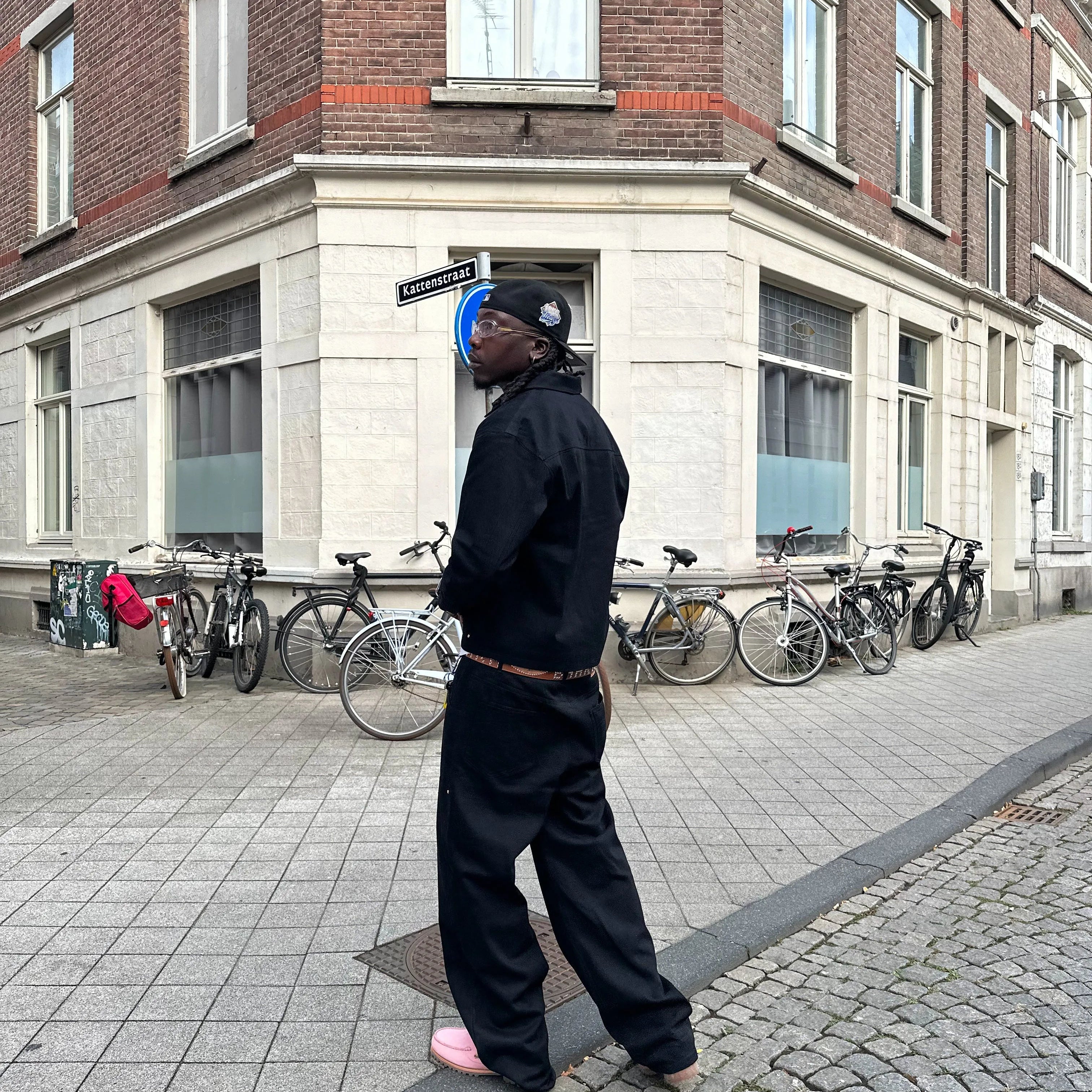 Person standing on a street with bicycles parked against a building.