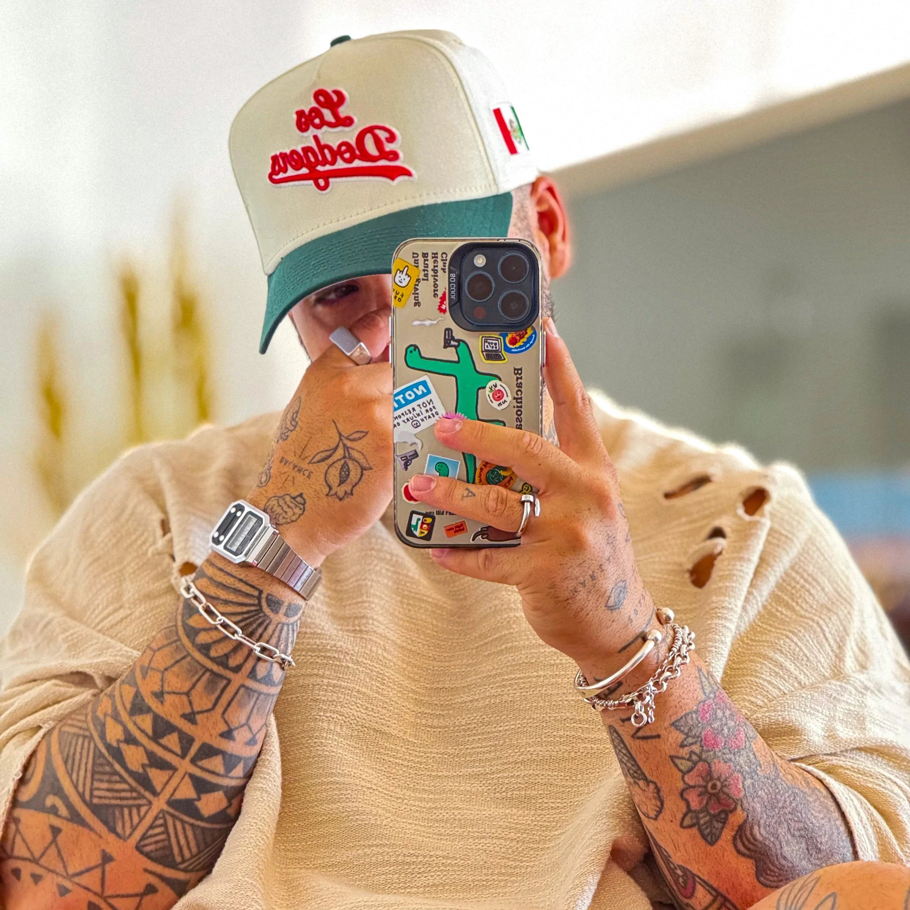 Person wearing a cap and holding a phone with a colorful case, sitting indoors