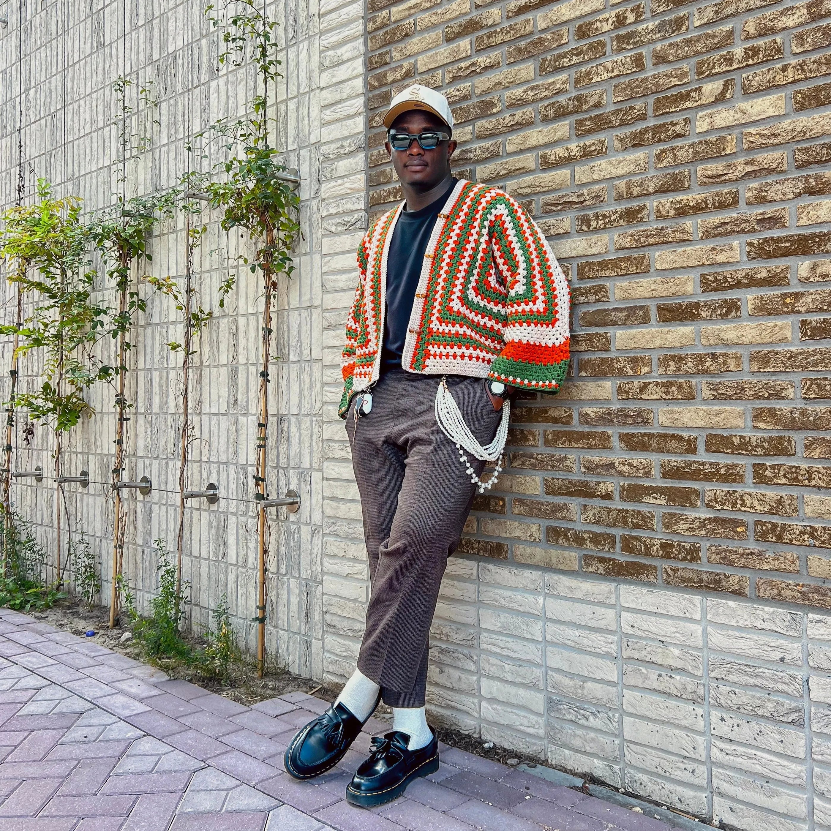Person wearing a colorful patterned cardigan leaning against a brick wall.