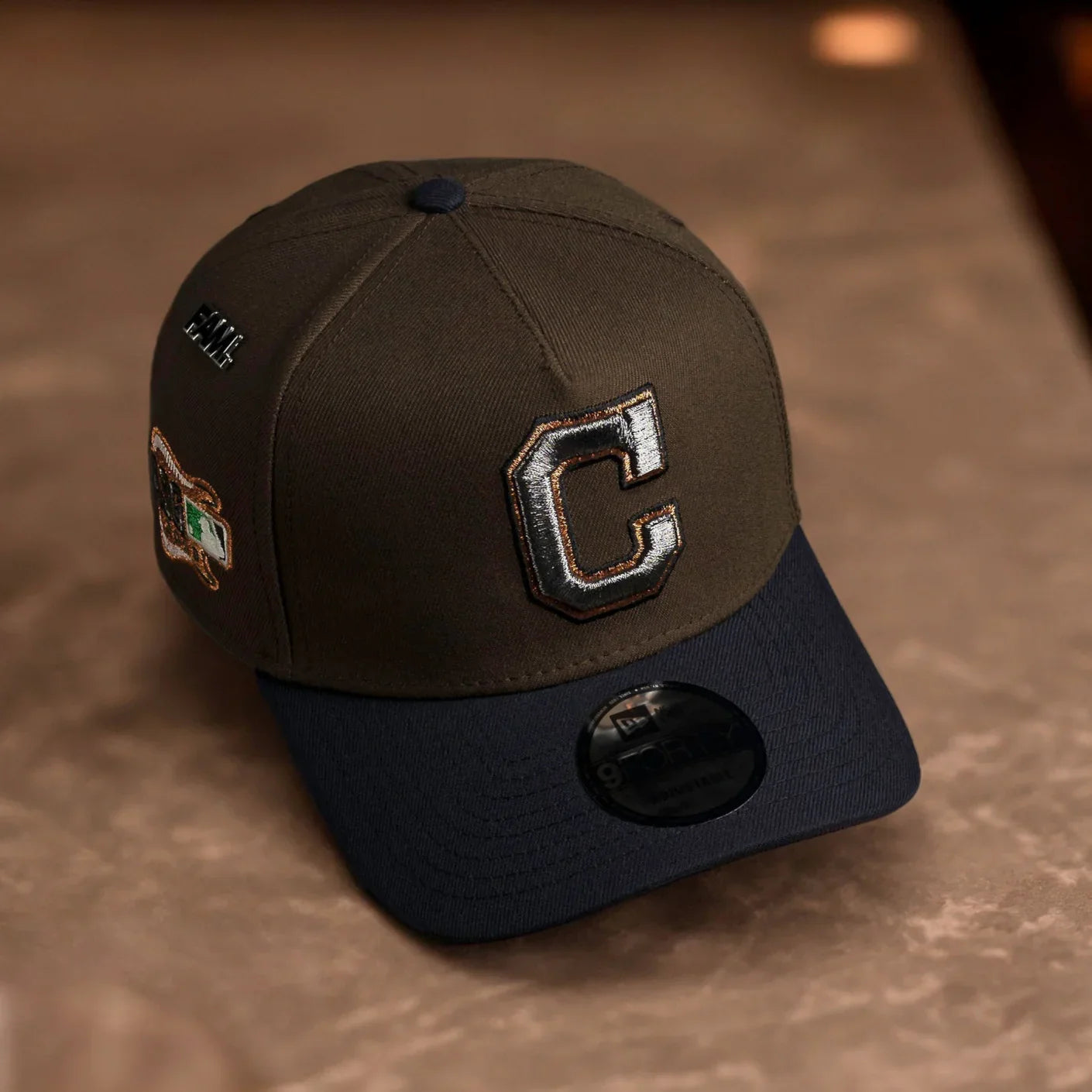Brown and black cap with a large 'C' logo on a brown surface